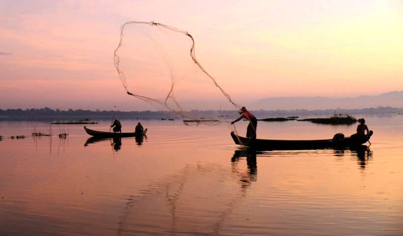 Fisherman throwing net into body of water